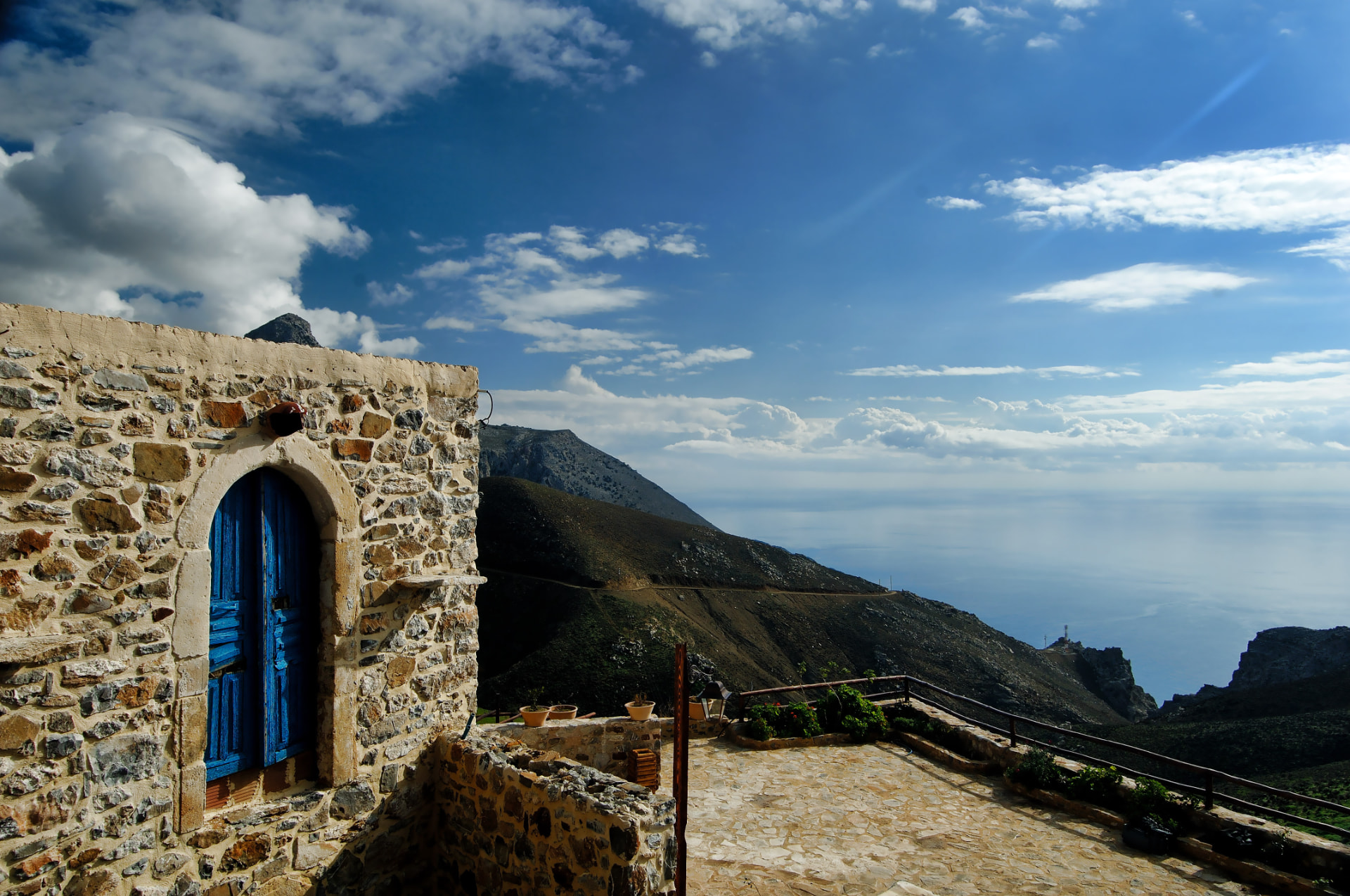 A blue wooden door in a stone wall with the sea beyond